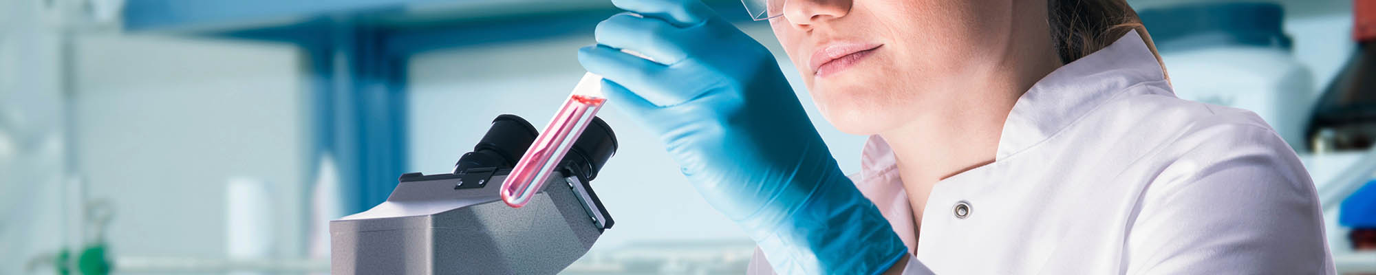 A scientist holds a test tube whilst sitting in front of a microscope