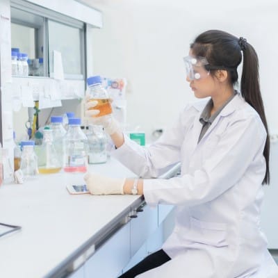 Female scientist holding beaker with orange clear liquid inside